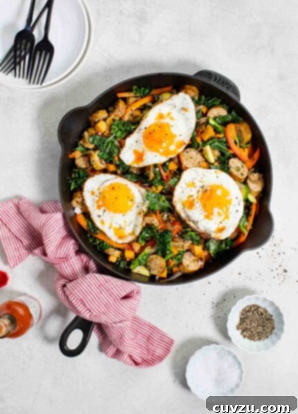 A cast-iron skillet filled with sweet potato and chicken sausage hash, topped with three fried eggs.