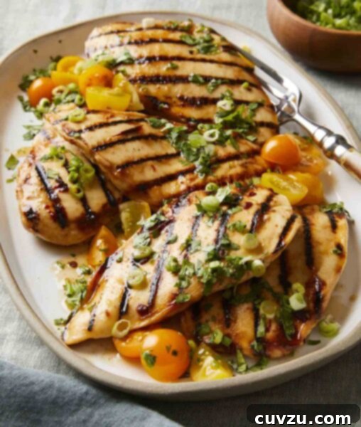 Five chicken breast pieces with grill marks on a platter, topped with halved cherry tomatoes, scallions, and cilantro.
