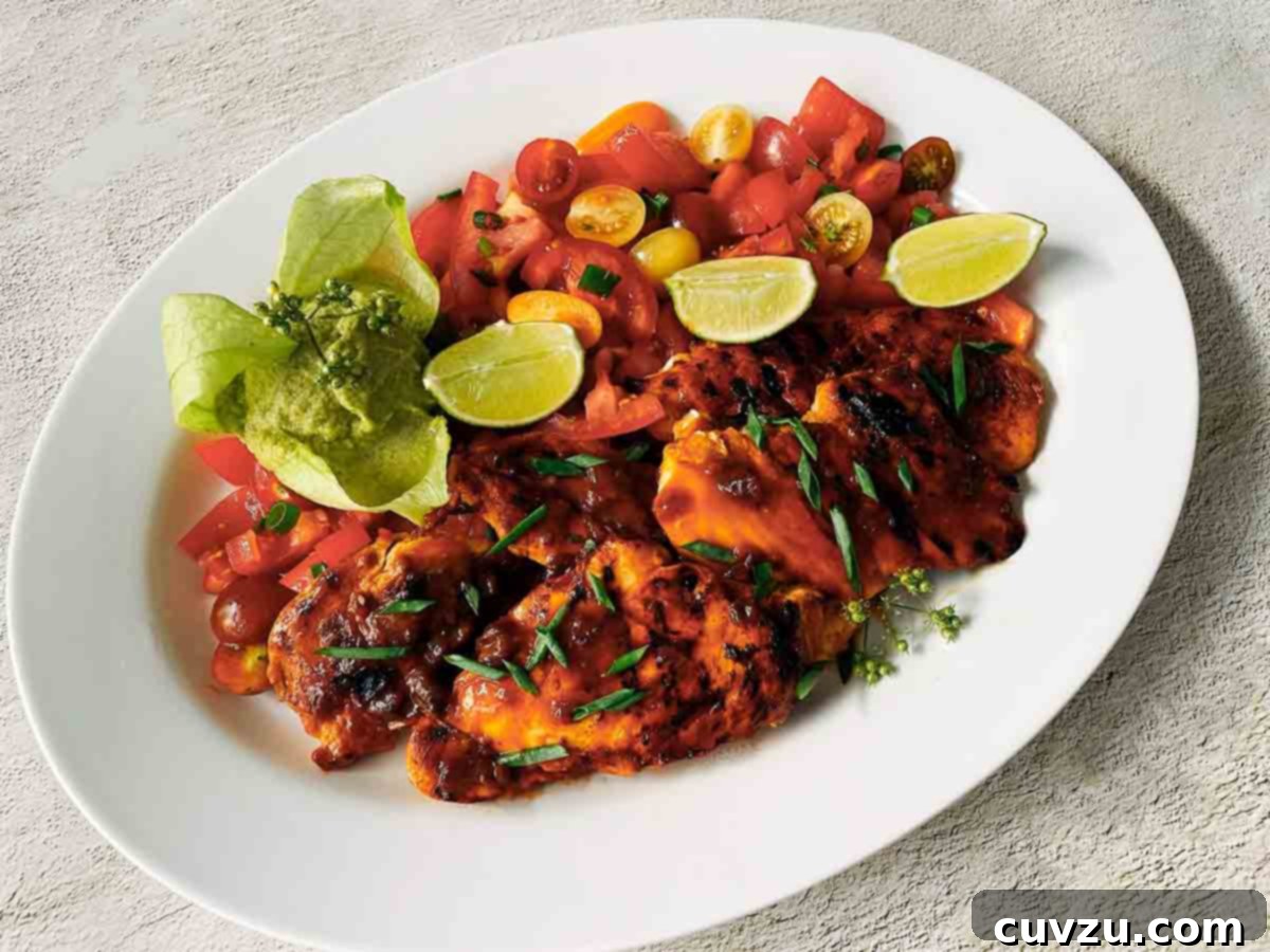 Honey-Glazed Chili-Lime Chicken 5 A white platter filled with marinated chicken breasts, tomato salad, and lime wedges.