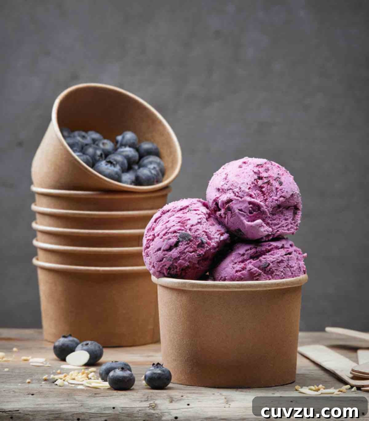Arctic Blueberry Delight 3 A close-up of three scoops of blueberry ice cream, showing its rich texture and beautiful purple hue, set against a blurred background of stacked containers.