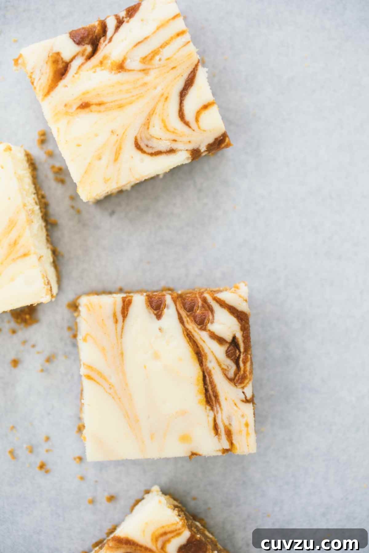 Four pumpkin swirl cheesecake bars on a white surface.