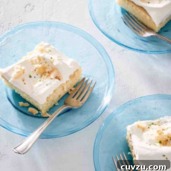 Tropical Coconut Tres Leches 3 Three pieces of white cake topped with frosting and toasted coconut on individual blue glass plates with forks resting on the side.