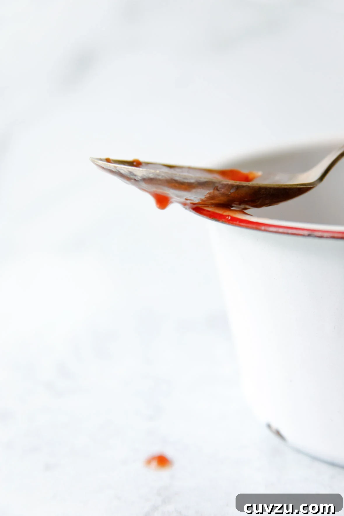 Crimson Delight 3 A spoon dripping with glossy, homemade strawberry jam, resting tantalizingly on the edge of an enamel pot, showcasing its perfect consistency.