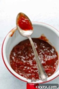 An enamel-coated pot filled with strawberry jam and a spoon resting on top.