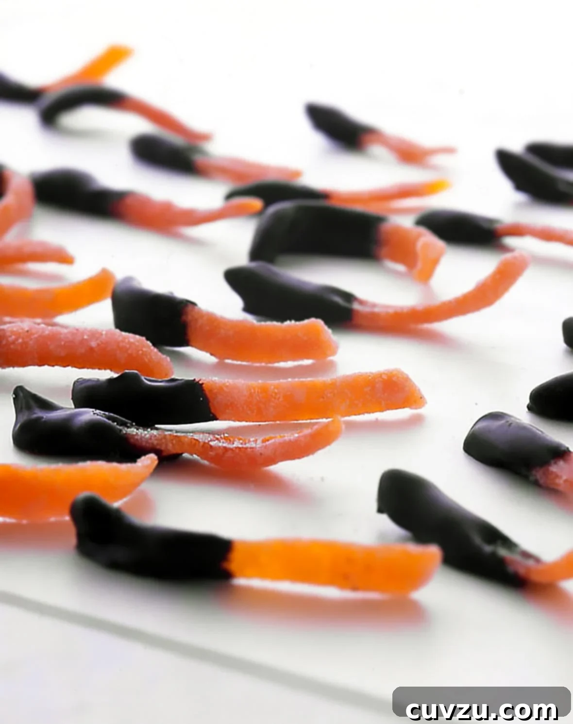 Bittersweet Chocolate Citrus Twists 2 Strips of chocolate dipped candied orange peel on a white surface, showcasing their elegant presentation and tempting texture.