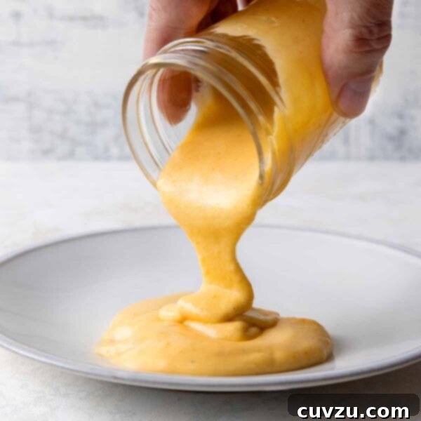 Golden Cheddar Drizzle 10 A person pouring Cheddar cheese sauce from a jar into a shallow bowl.