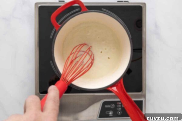 Golden Cheddar Drizzle 15 A person whisking a roux in a saucepan.