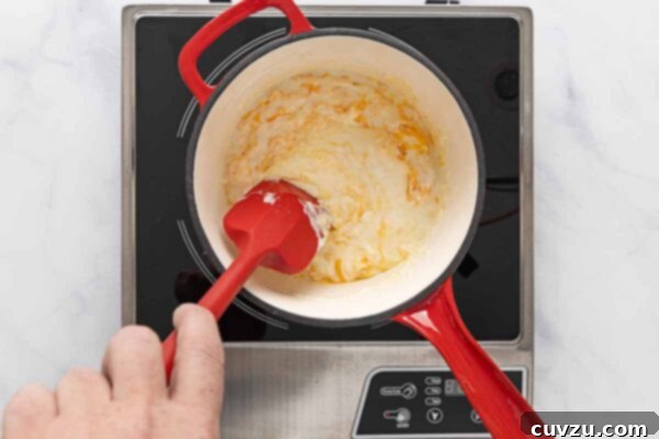Golden Cheddar Drizzle 16 A creamy cheese sauce mixture being stirred in a saucepan.