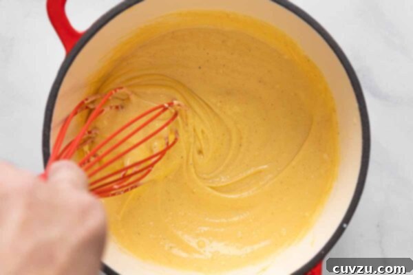 Golden Cheddar Drizzle 17 Cheese sauce being whisked in a saucepan.