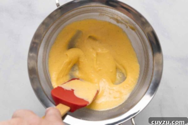 Golden Cheddar Drizzle 18 Cheese sauce being strained through a fine mesh sieve.