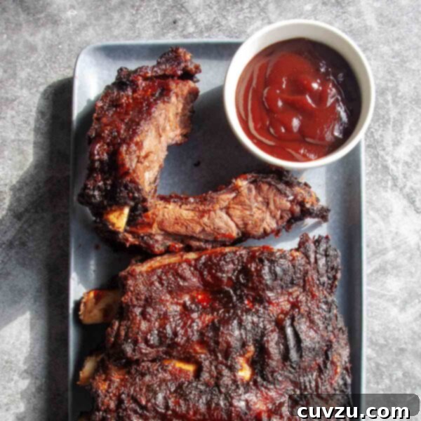 Slow-Smoked Beef Back Ribs 8 A rack of barbecued beef back ribs on a rectangular platter with a dish of barbecue sauce on the side.