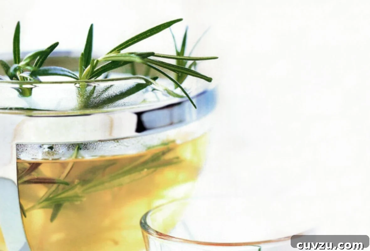 Herbal Rosemary Elixir 2 A pot of rosemary infused tea with rosemary sprigs sticking out the top and a glass beside it, inviting warmth and relaxation.