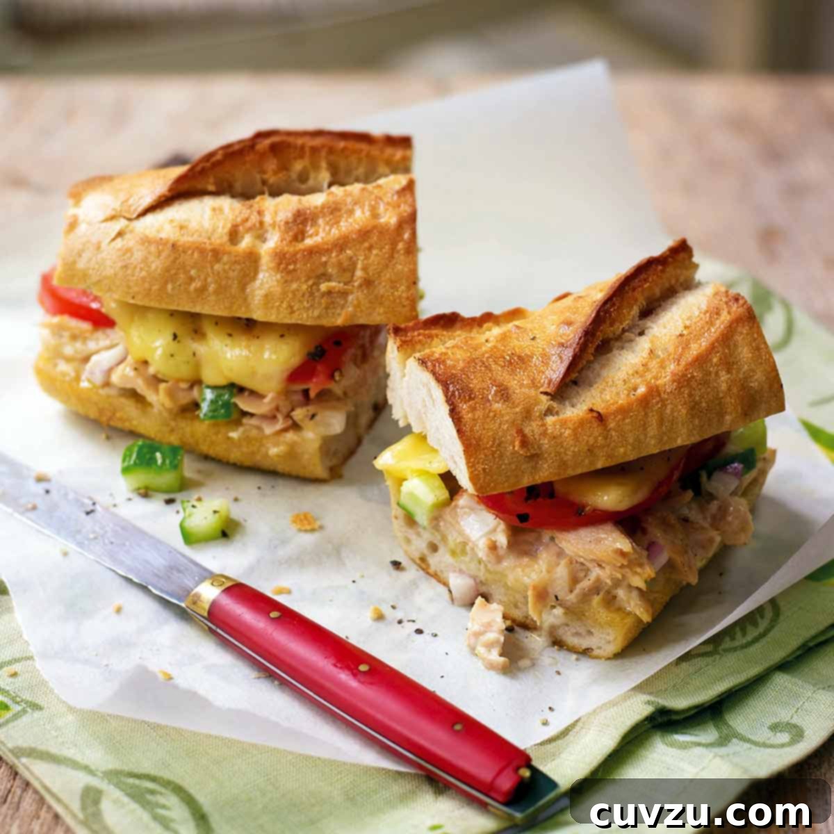 A halved fancy tuna melt with tomato and cucumber on a baguette on a piece of parchment.