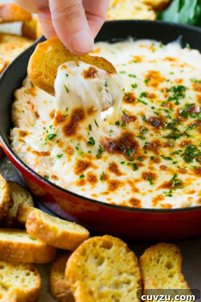 A person using a crispy baguette slice to scoop out shrimp scampi dip from a bowl.