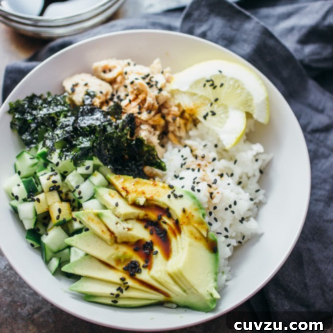 A white. bowl filled with sliced avocado, rice, lemon, canned tuna, seaweed, cucumber, and black sesame seeds.