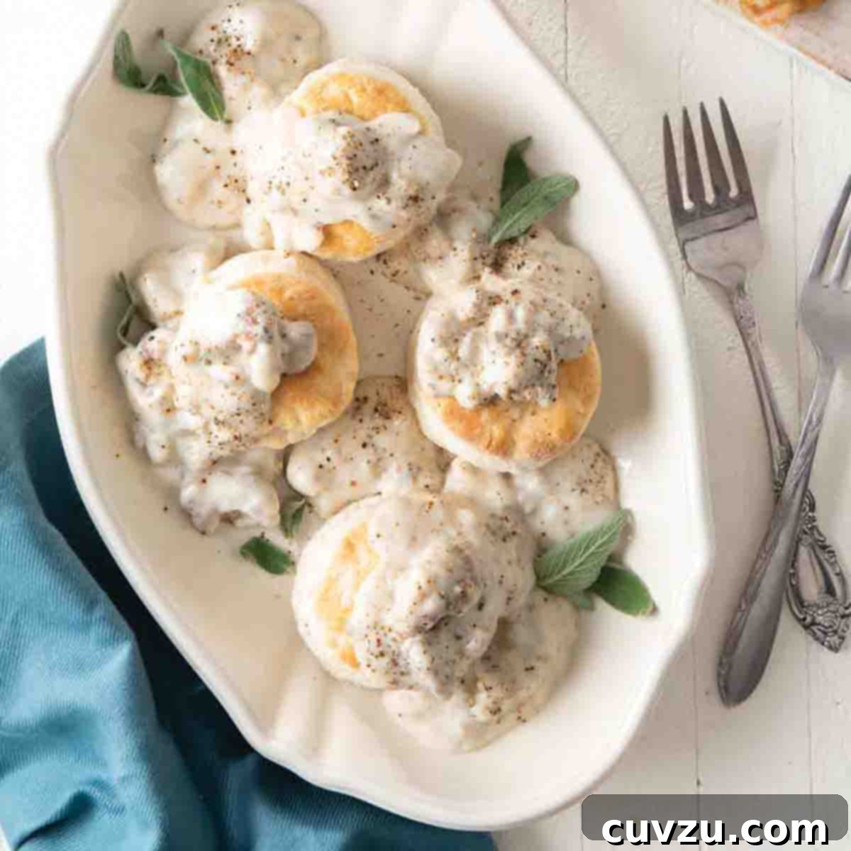 A serving platter with four cat head biscuits and gravy and sage leaves to garnish.