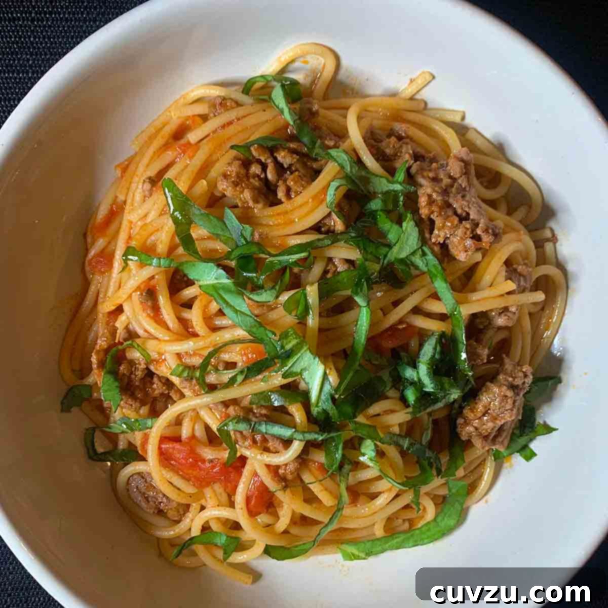 Easy One Pot Spaghetti Dinner 10 A white bowl filled with spaghetti and meat sauce with a basil chiffonade on top.