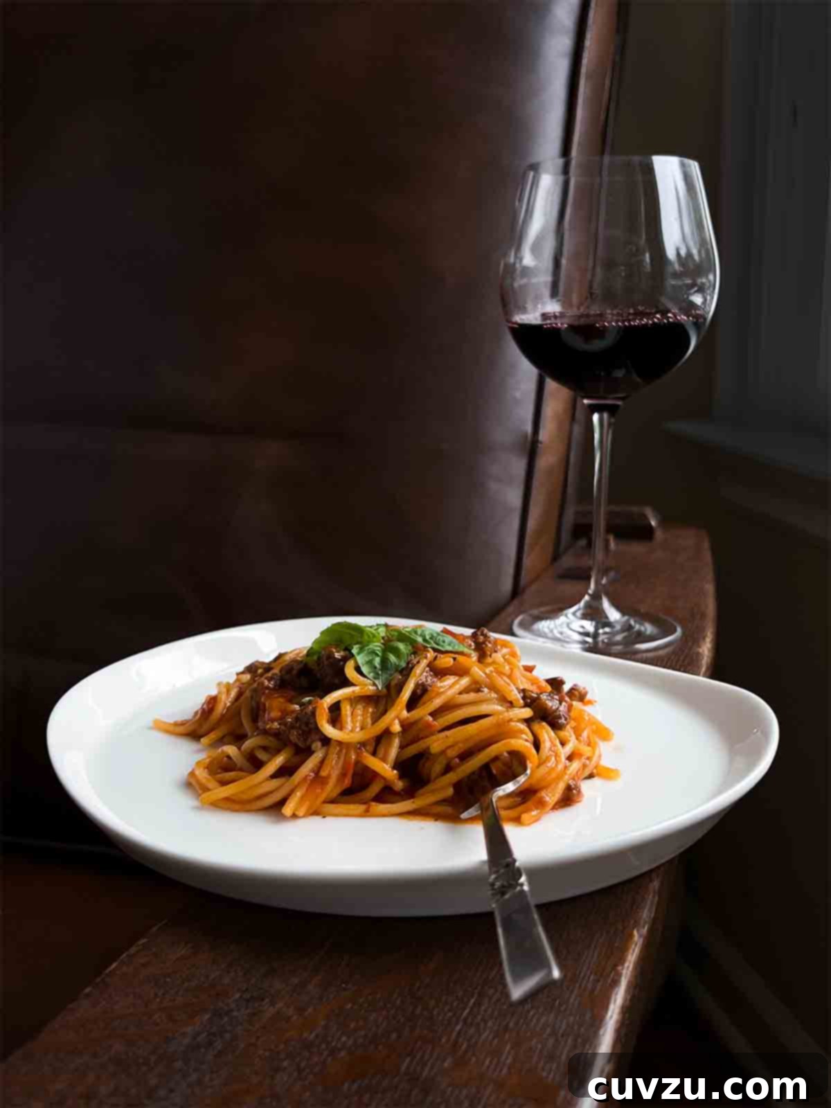 Easy One Pot Spaghetti Dinner 6 A plate of one-pot spaghetti and meat sauce, topped with fresh basil, and a glass of wine in the background.