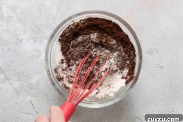 Irresistible Chocolate Muffins 12 A person whisking flour, cocoa, and sugar together in a bowl.
