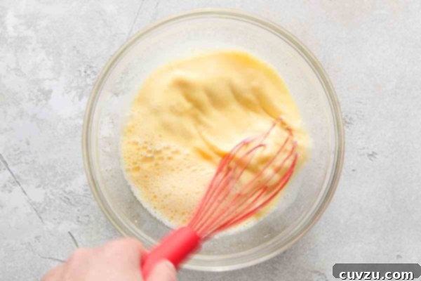 Irresistible Chocolate Muffins 14 A person whisking eggs and milk together in a glass bowl.