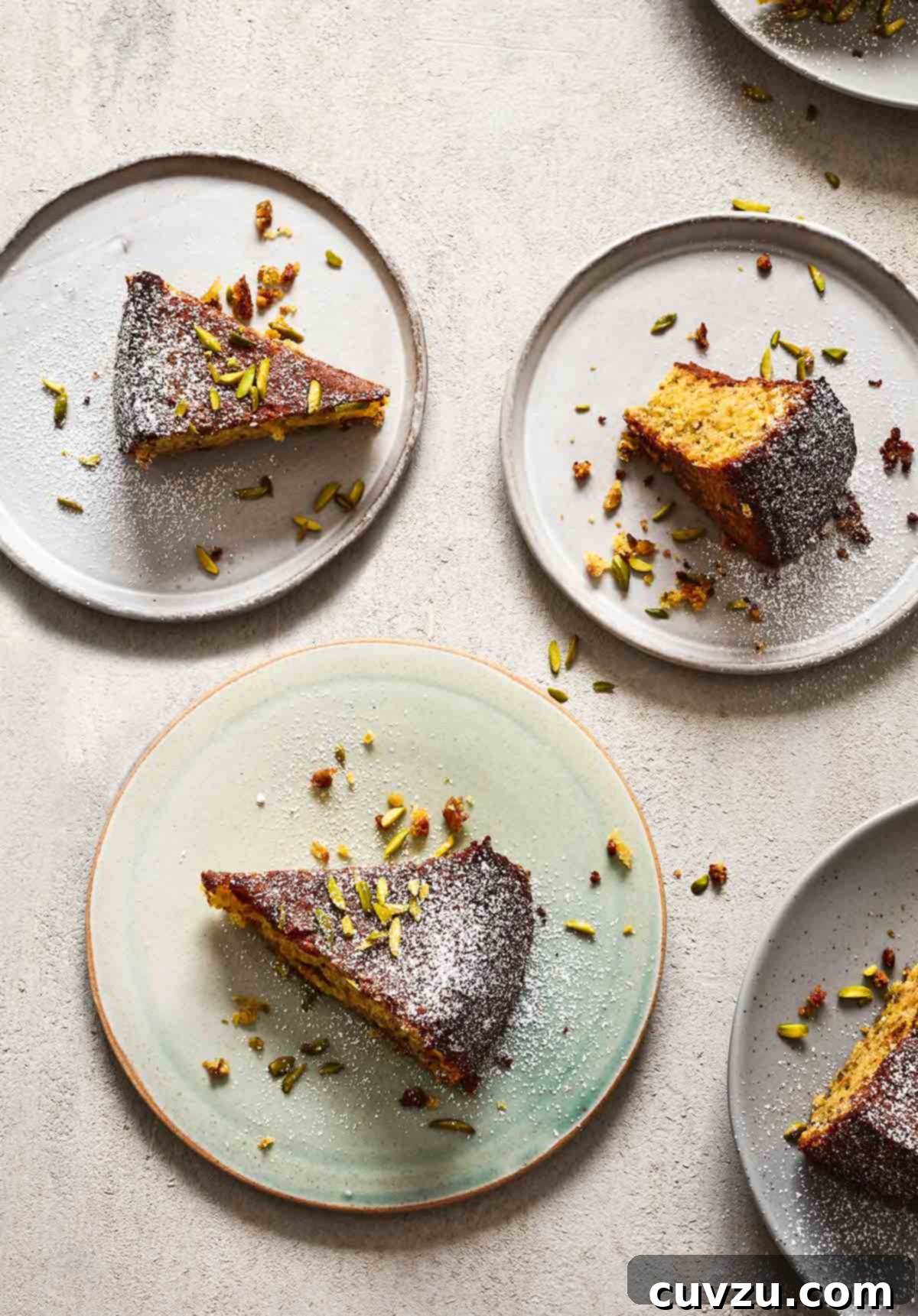 Several plates with slices of pistachio-lime polenta cake topped with confectioners' sugar and chopped pistachios