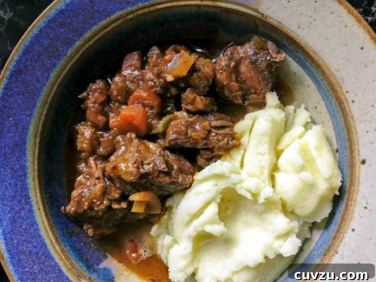 Hearty Slow Cooker Irish Beef Stew 7 A bowl half filled with beef stew and half filled with mashed potatoes.