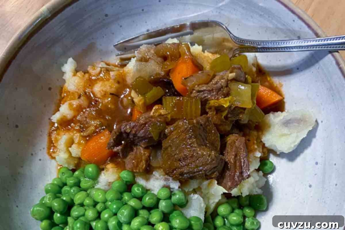 Hearty Slow Cooker Irish Beef Stew 8 A bowl filled with mashed potatoes topped with beef stew and peas on the side.