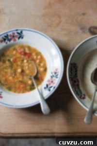 Cozy Smoked Paprika Chickpea Soup 2 Two bowls, one filled with smoked paprika and chickpea soup, with a spoon resting inside, and the other bowl empty.