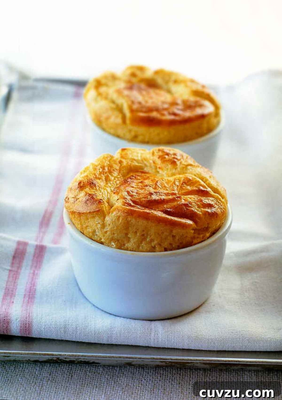 13 Recipes to Make Mom's Day Unforgettable 7 Two puffy, golden Parmesan and Gruyere Cheese Souffles in white bowls on a towel.