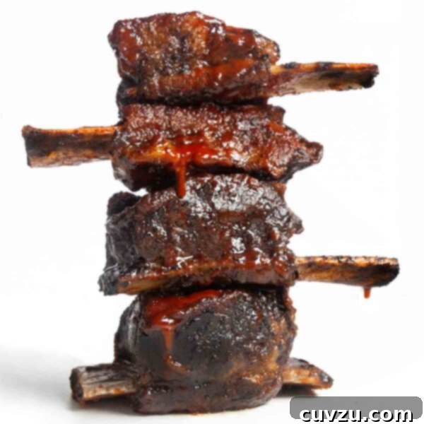 Four grilled short ribs in a stack on a white background, showcasing their smoky char and sticky glaze.