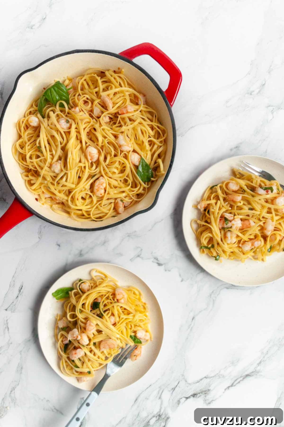 An overhead view of a skillet of shrimp pasta with a serving spoon, and two plates nearby filled with the delicious garlic butter shrimp pasta.