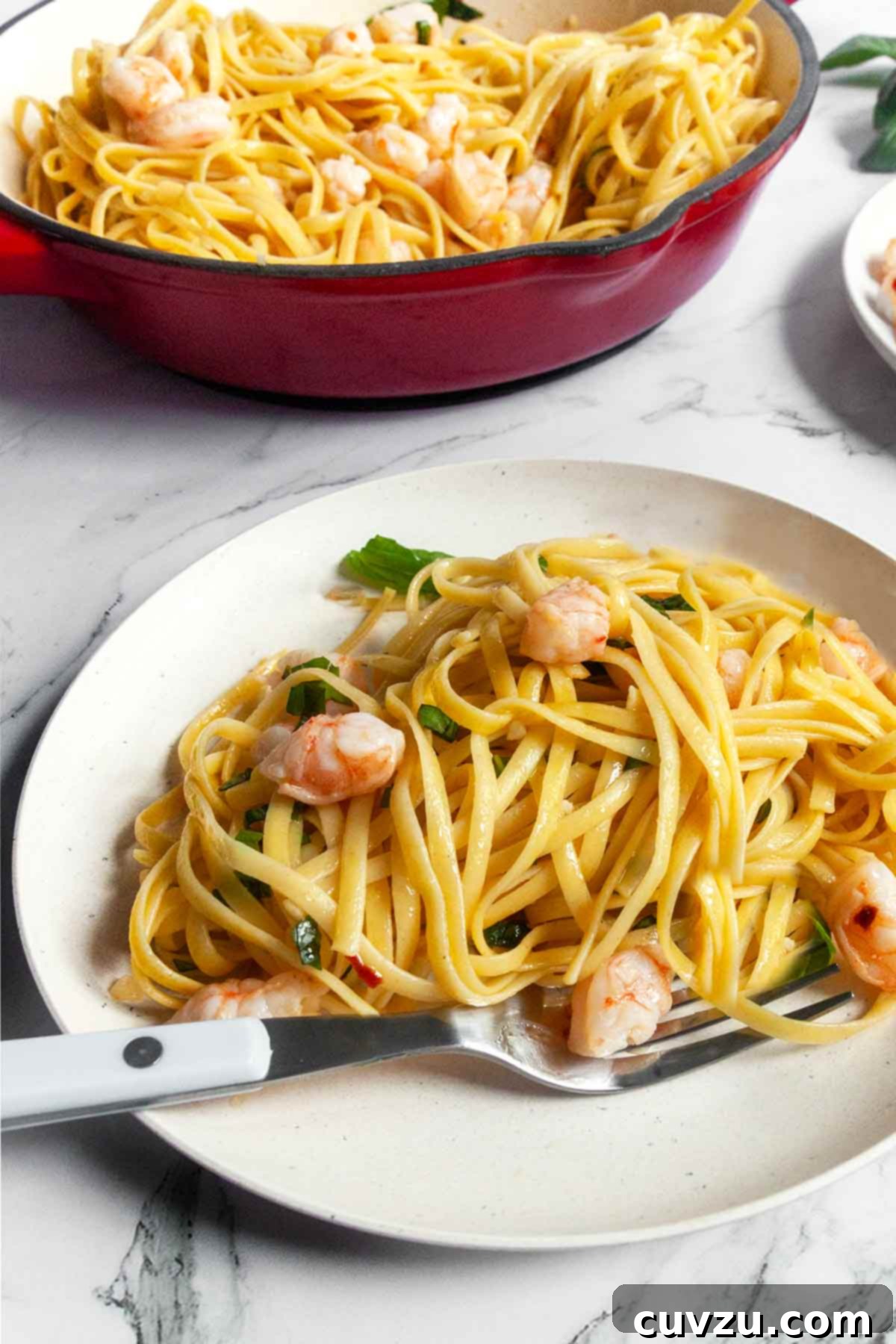 A beautifully plated serving of garlic shrimp linguine with a fork, and the skillet of pasta in the softly blurred background.