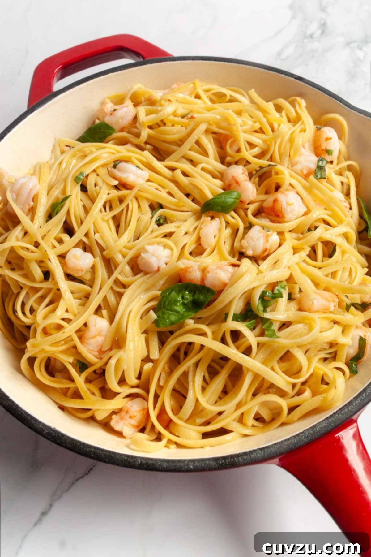 A vibrant close-up of garlic shrimp pasta, freshly tossed with basil, nestled in a red enamel skillet.