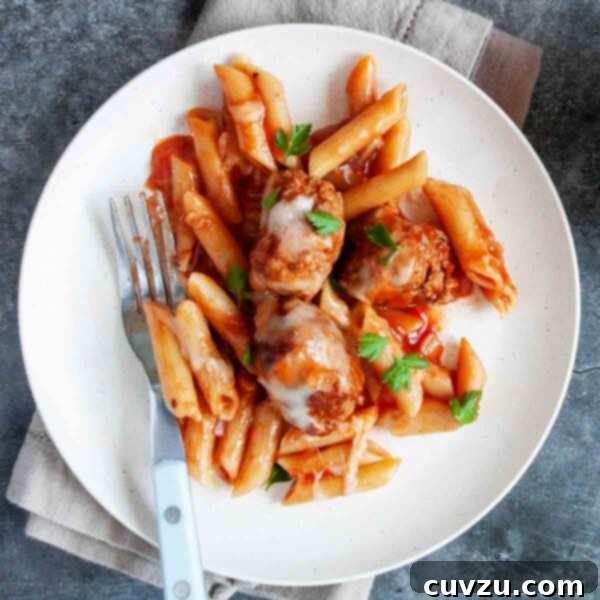 A white plate topped with penne, meatballs, and fresh parsley.