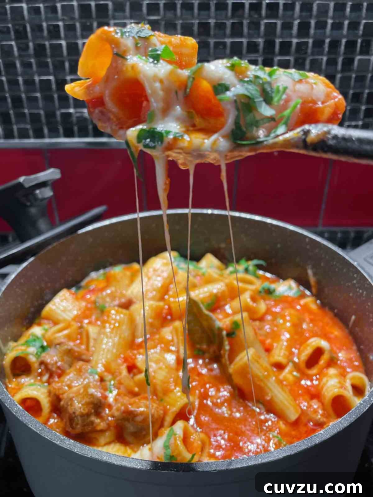 Easy One-Pot Sausage Meatball Pasta 11 A scoop of rich one-pot pasta and tomato sauce, laden with mini meatballs, being carefully lifted from a bubbling pot, showcasing the creamy, starchy texture of the dish.