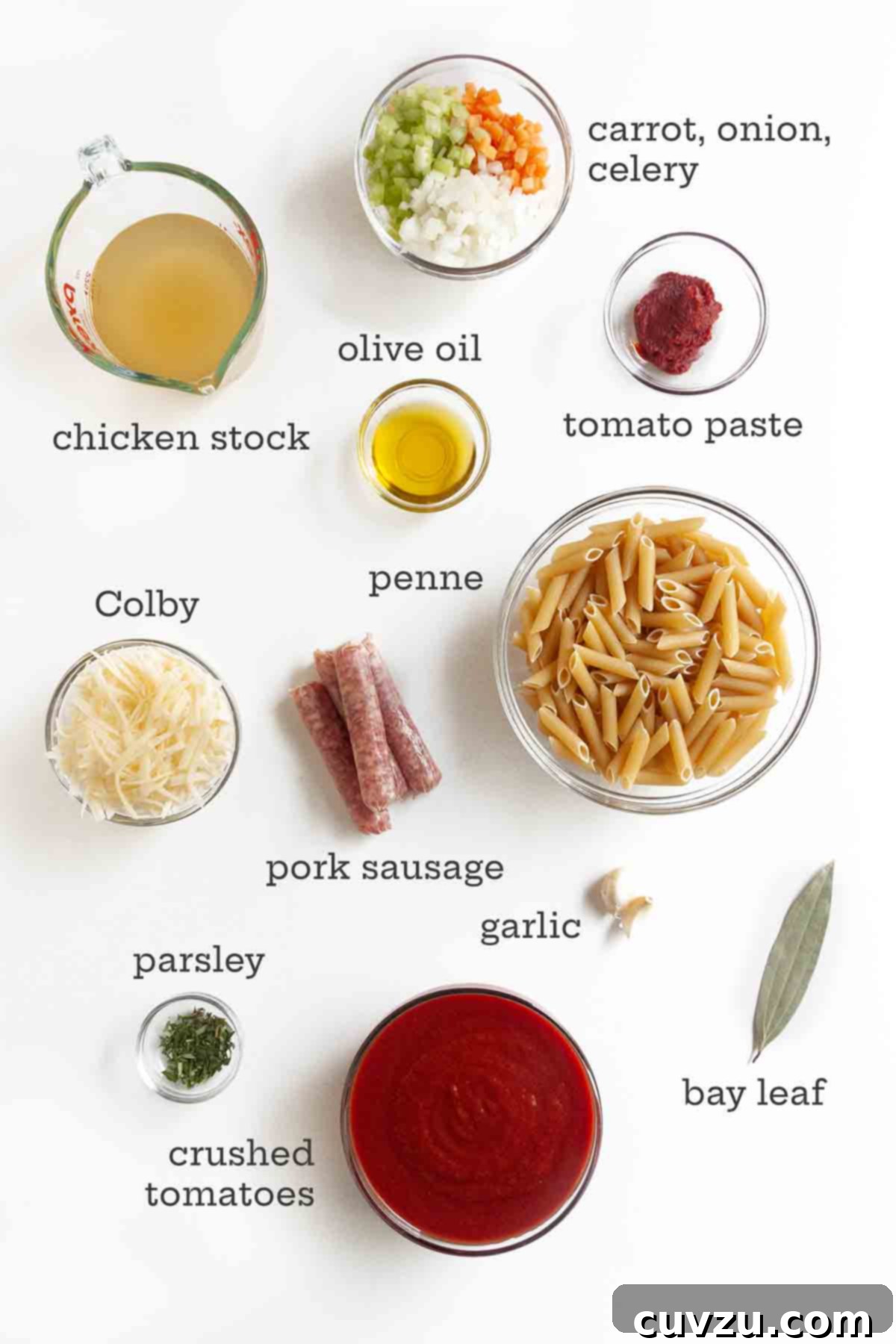 Easy One-Pot Sausage Meatball Pasta 4 A carefully arranged spread of ingredients for one-pot pasta with sausage meatballs, including pasta, fresh vegetables, uncooked sausage, chicken stock, crushed tomatoes, tomato paste, cheese, garlic, and a bay leaf, ready for preparation.