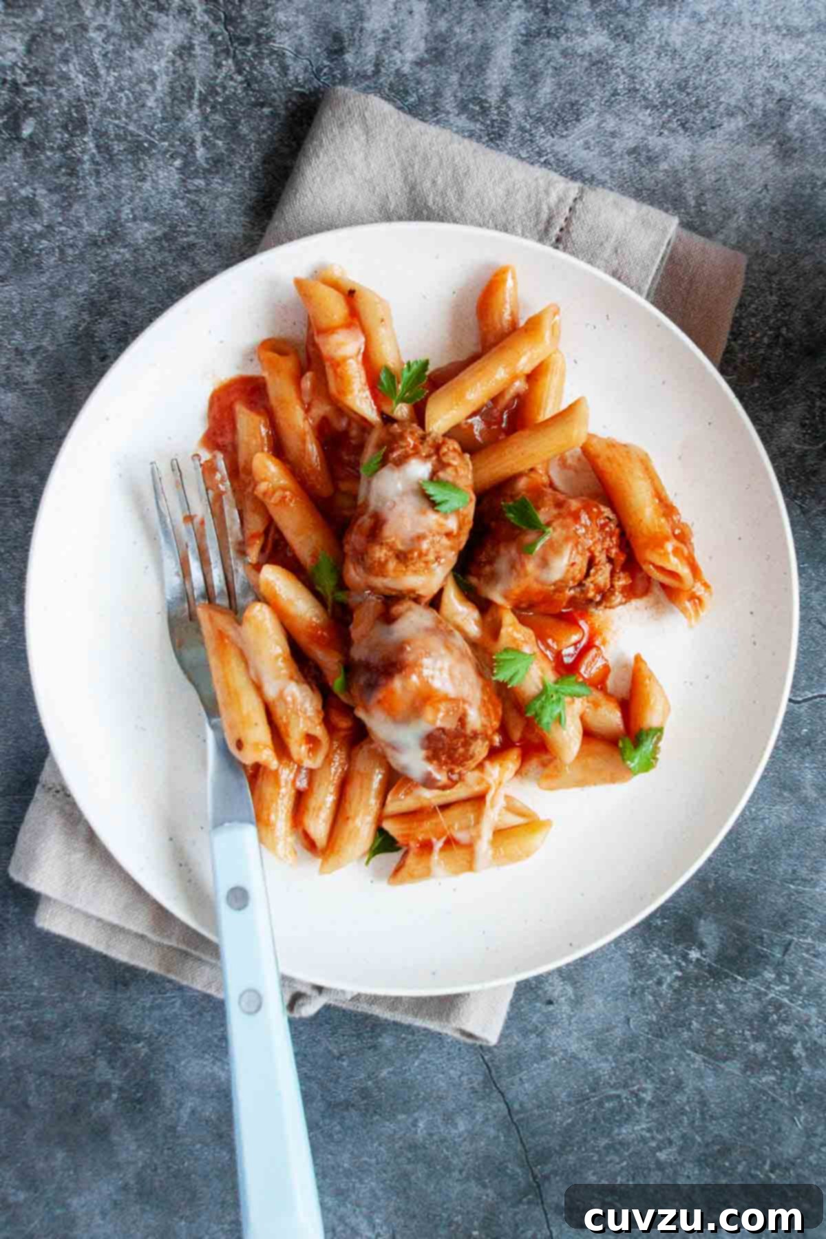 Easy One-Pot Sausage Meatball Pasta 8 A perfectly portioned white plate showcasing a serving of penne pasta, succulent sausage mini meatballs, and rich tomato sauce, garnished with fresh, finely chopped parsley.