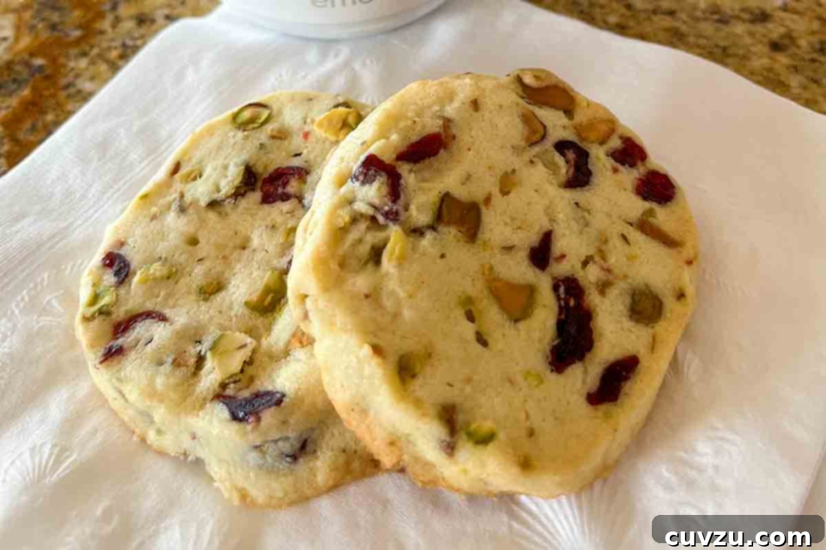 Jewel Toned Pistachio Cookies 13 Two exquisite cranberry pistachio cookies resting delicately on a crisp white napkin, highlighting their inviting textures.
