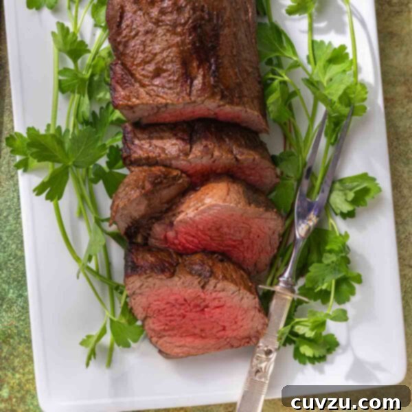 A sliced beef tenderloin on a white platter with sprigs of parsley.
