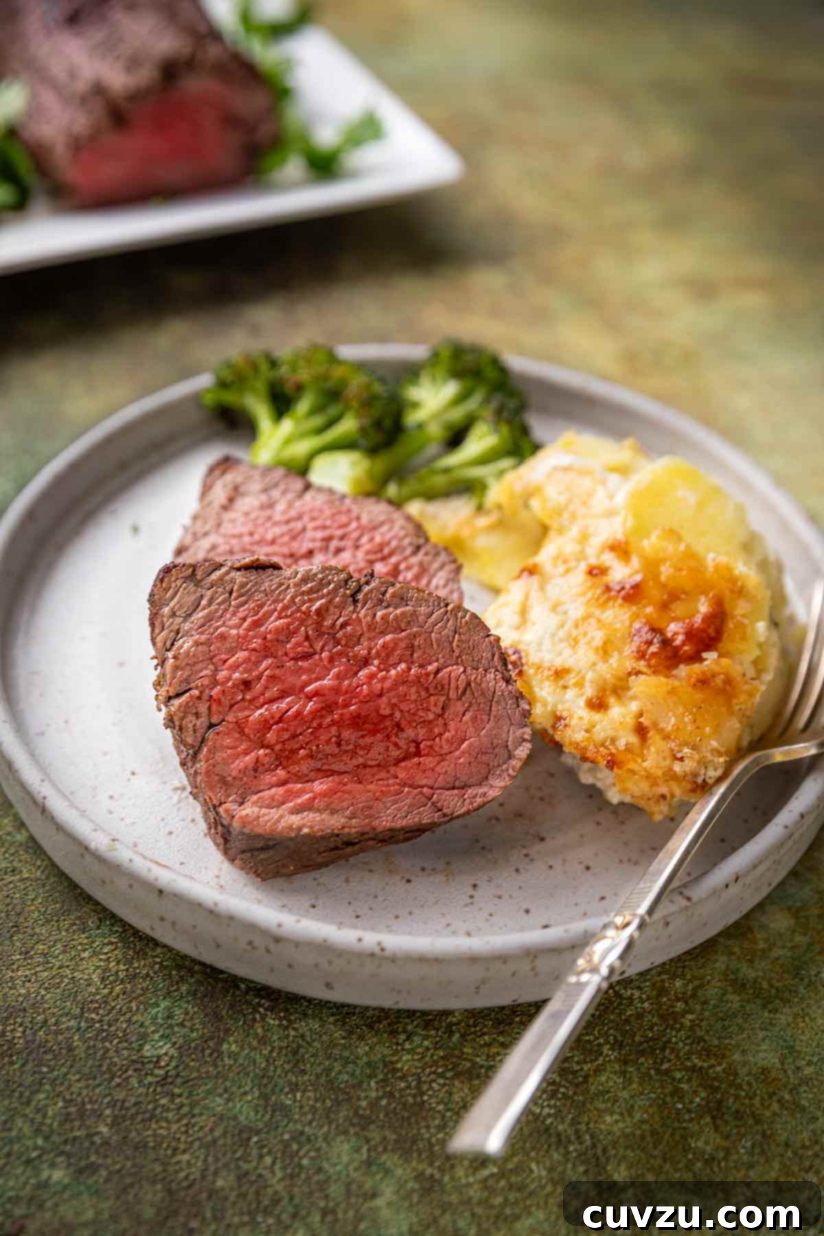 Aromatic Shawarma Beef Tenderloin Roast 7 Slices of spiced beef tenderloin roast served on a plate alongside cheesy potatoes and roasted broccoli florets.