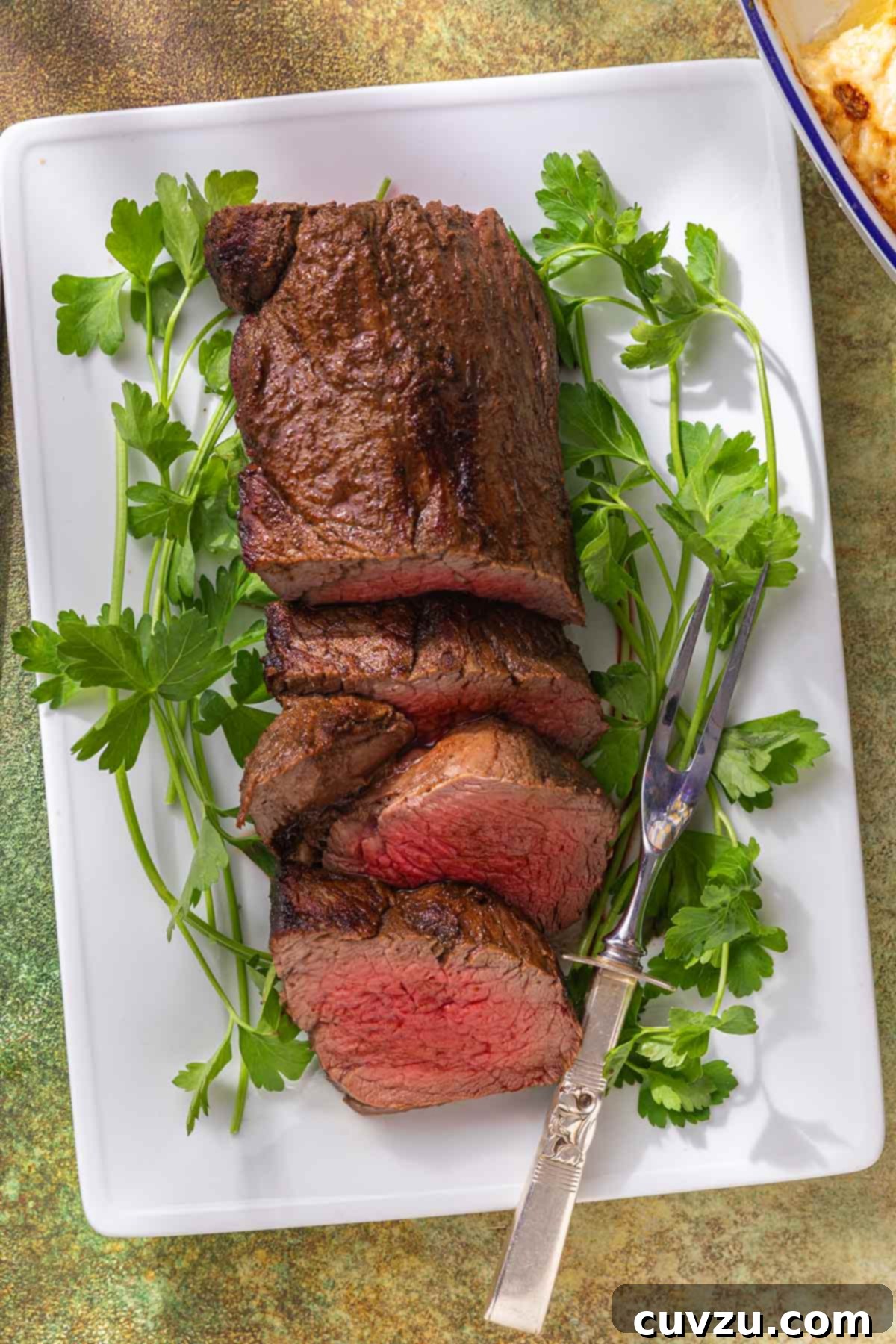 Aromatic Shawarma Beef Tenderloin Roast 8 A close-up shot of a sliced beef tenderloin roast, garnished with fresh parsley sprigs on a white serving platter, showcasing its tender texture and spiced crust.