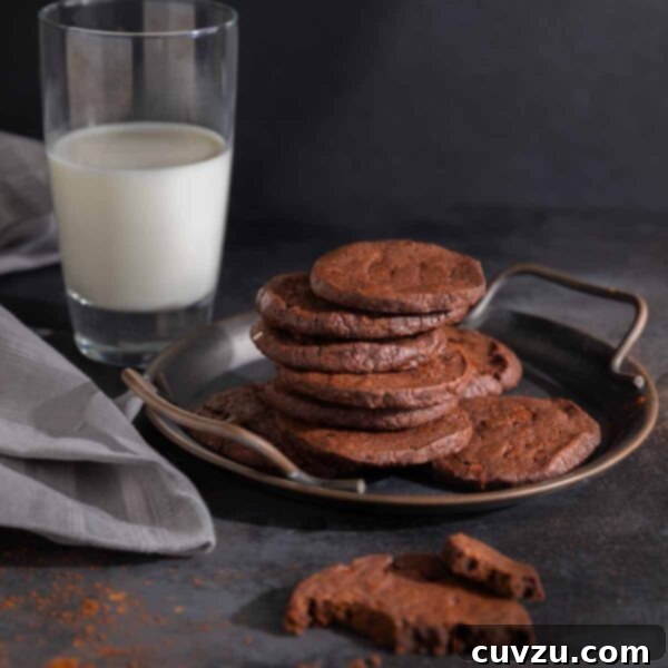 A metal tray with a pile of chocolate espresso shortbread cookies on it. Nearby, a glass of milk.
