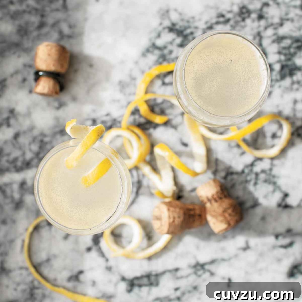 Two flutes filled with homemade sparkling juice topped with lemon twists on a marble surface.