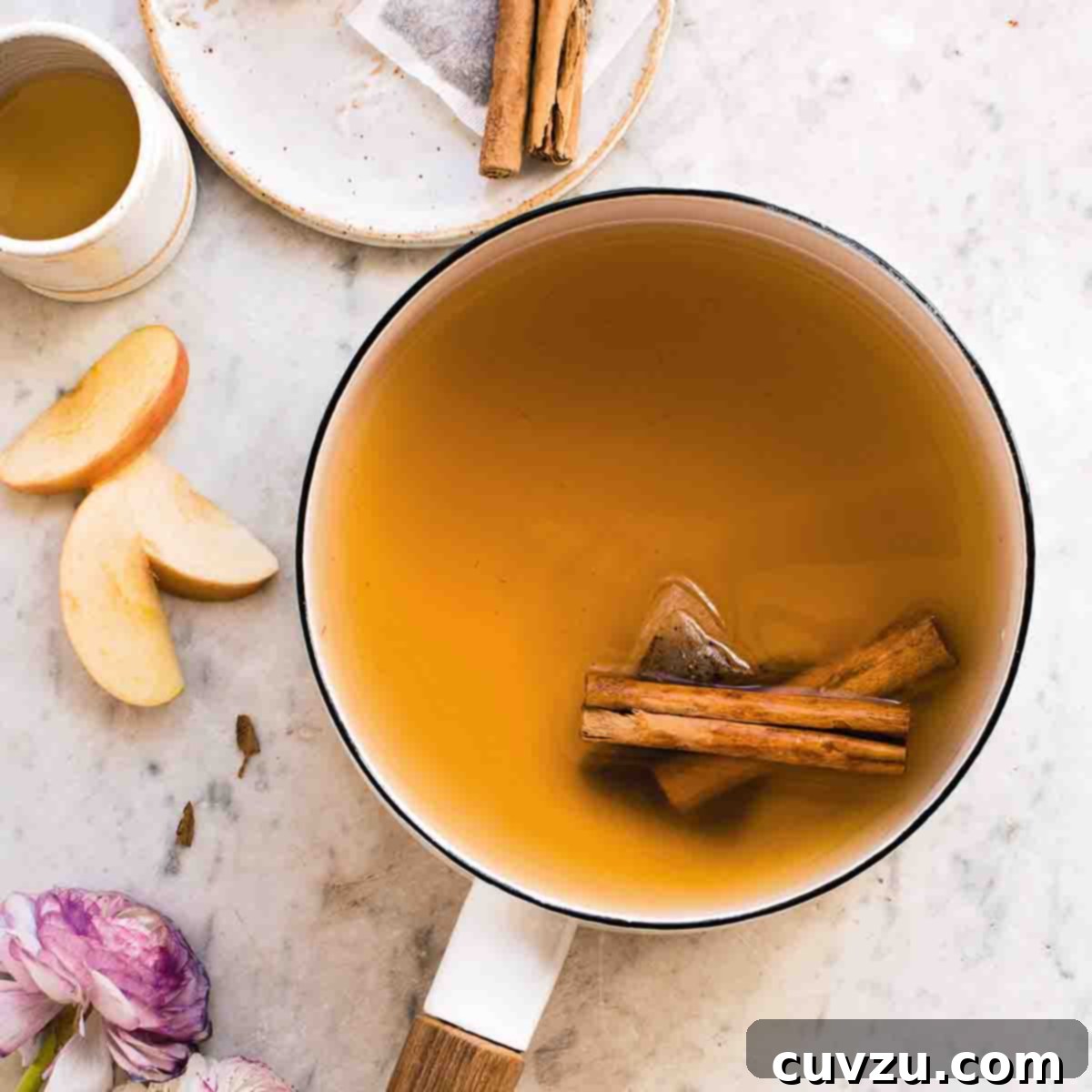 A white enamel pot filled with chai spiced apple cider and two cinnamon sticks.