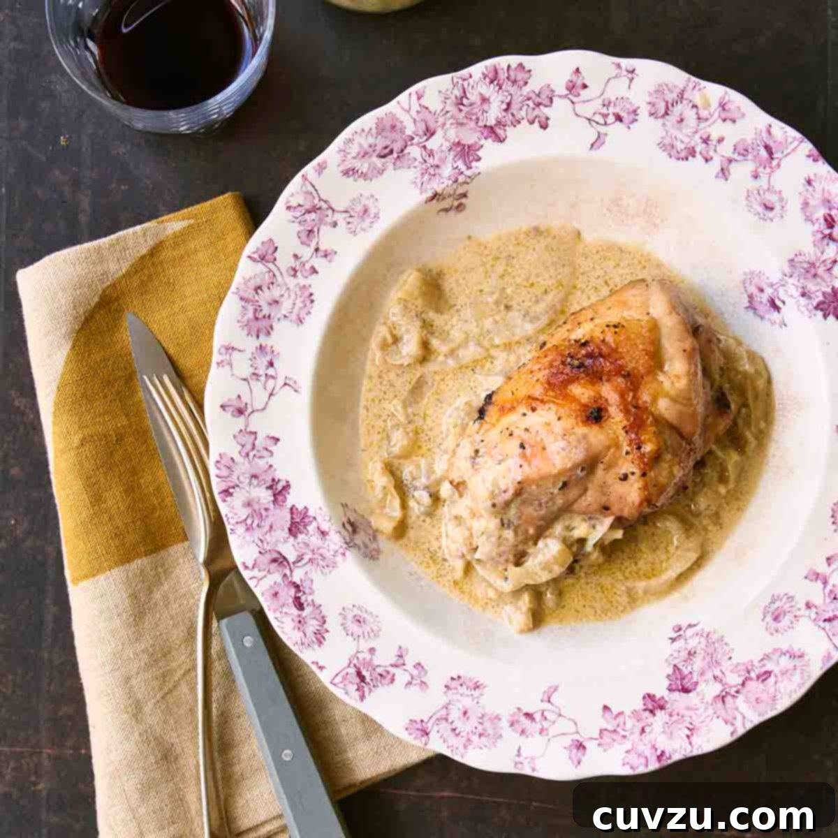 Six Flavorful Bone-In Chicken Breast Dinners 6 A floral-patterned plate topped with a piece of roast chicken with onion gravy around it and a fork, knife, and napkin on the side.