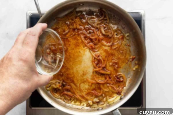 Velvety Meatball Stroganoff 15 White wine being poured into a skillet of sautéed onions.