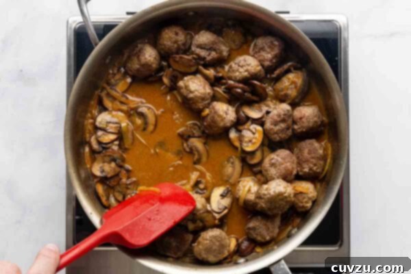 Velvety Meatball Stroganoff 17 A person stirring meatballs and mushrooms in a skillet.