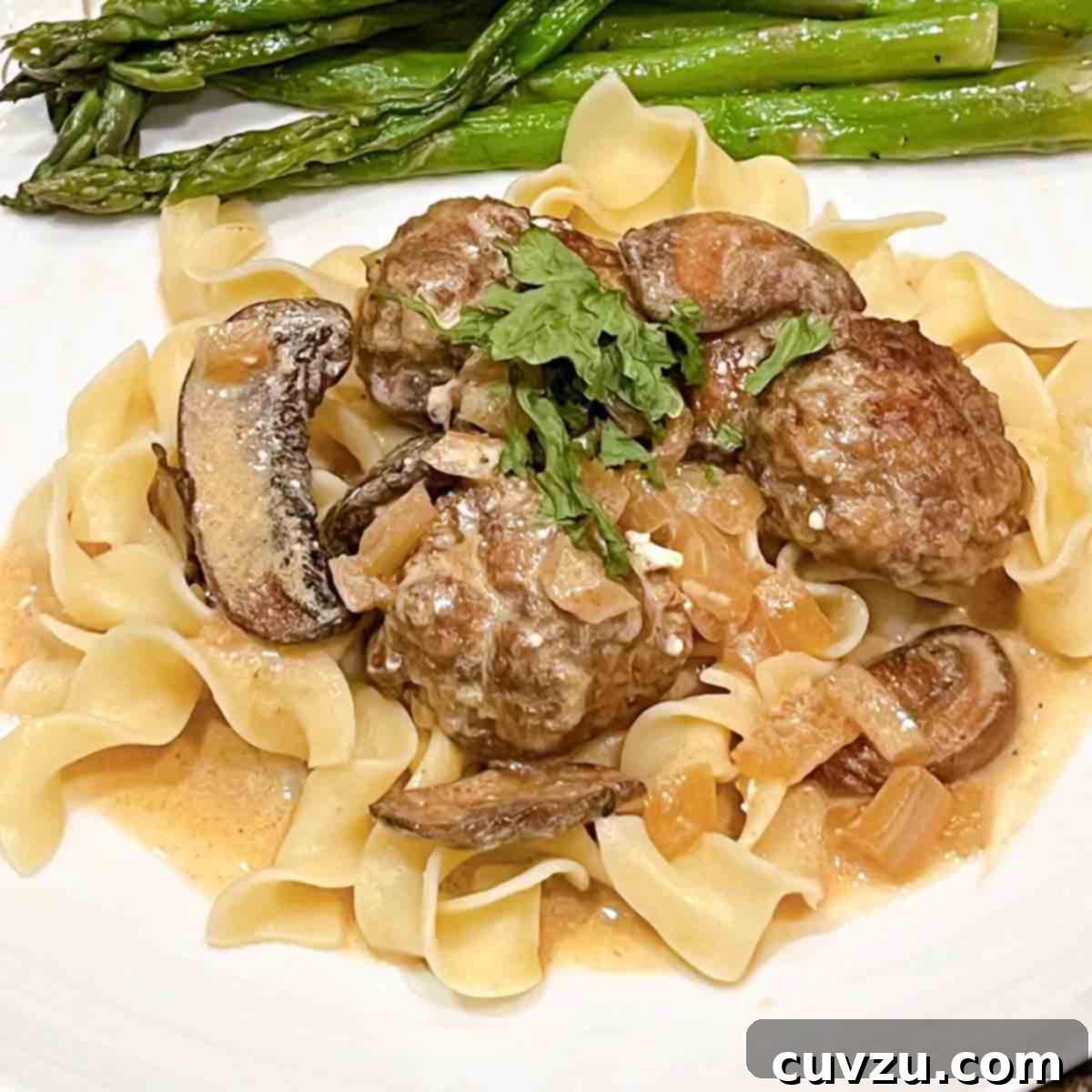 Velvety Meatball Stroganoff 20 A plate of egg noodles topped with meatball stroganoff and asparagus on the side.