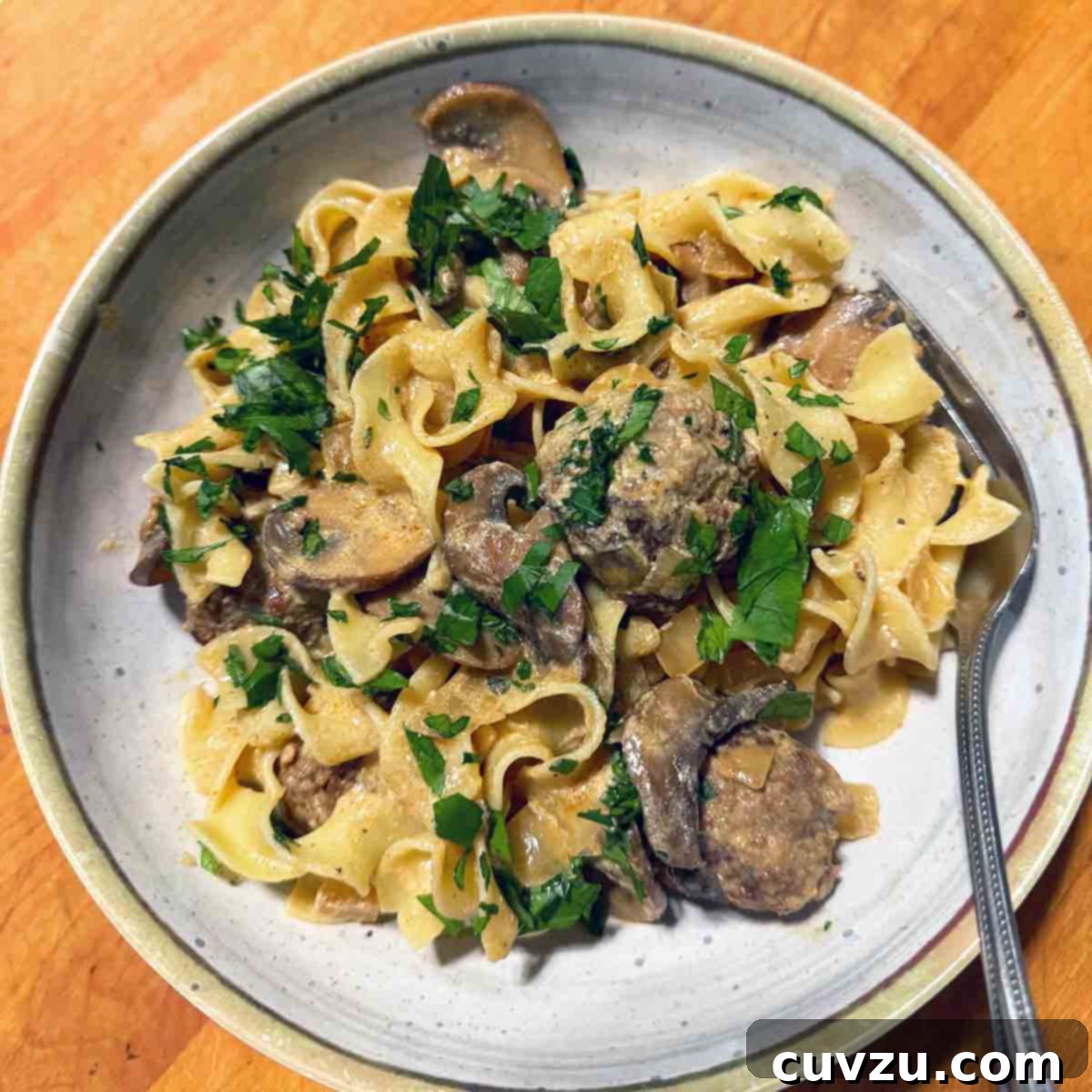 Velvety Meatball Stroganoff 21 A plate egg noodles topped with meatball stroganoff and garnished with chopped parsley.