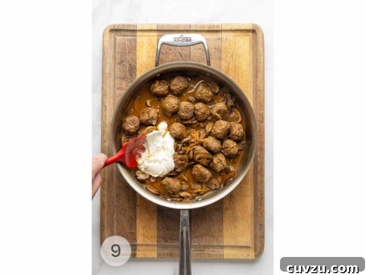 Velvety Meatball Stroganoff 8 A skillet filled with meatball Stroganoff and a spatula stirring in sour cream.